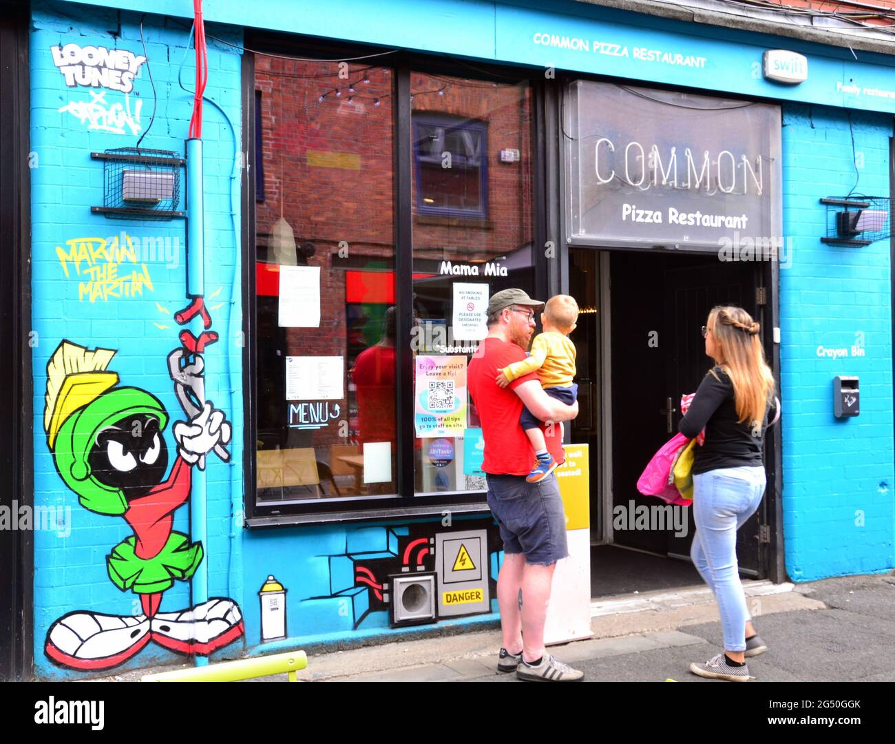 Mann, Frau und Baby stehen neben einem Bild von Marvin, der Zeichentrickfigur des Mars, Teil eines Looney Tunes Kunstpfades, der in Manchester, England, Großbritannien, eröffnet wurde. Der Weg wird den Film Space Jam: A New Legacy markieren, der in Kürze in den Kinos in Manchester zu sehen sein wird. Die Cartoon-Bilder erscheinen an 12 Orten in Manchester. Dies auf der Edge Street. Stockfoto