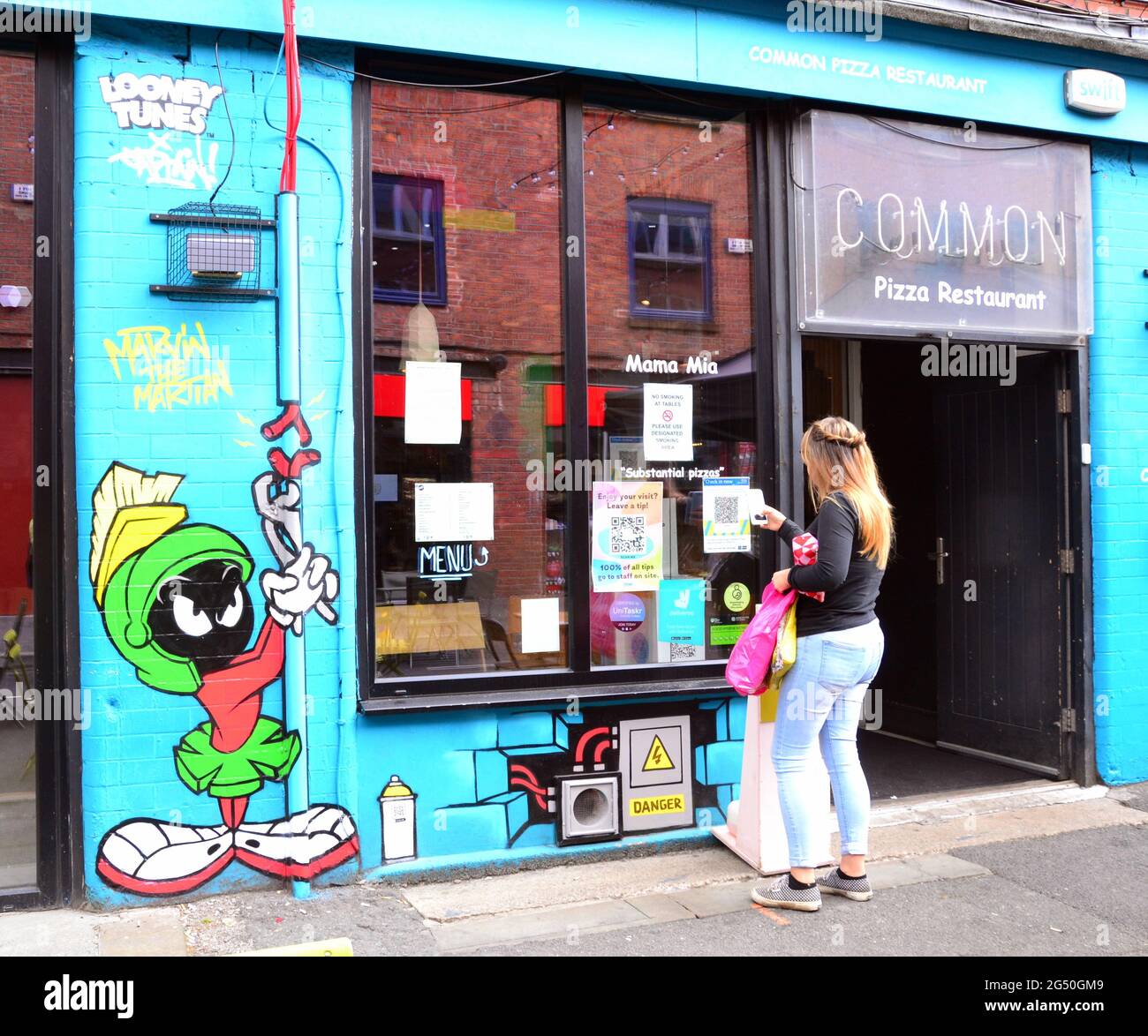 Eine Frau steht neben einem Bild von Marvin, dem Zeichentrickfilm des Mars, der Teil eines Looney Tunes-Kunstpfades ist, der in Manchester, England, Großbritannien, eröffnet wurde. Der Weg wird den Film Space Jam: A New Legacy markieren, der in Kürze in den Kinos in Manchester zu sehen sein wird. Die Cartoon-Bilder erscheinen an 12 Orten in Manchester. Dies auf der Edge Street. Stockfoto
