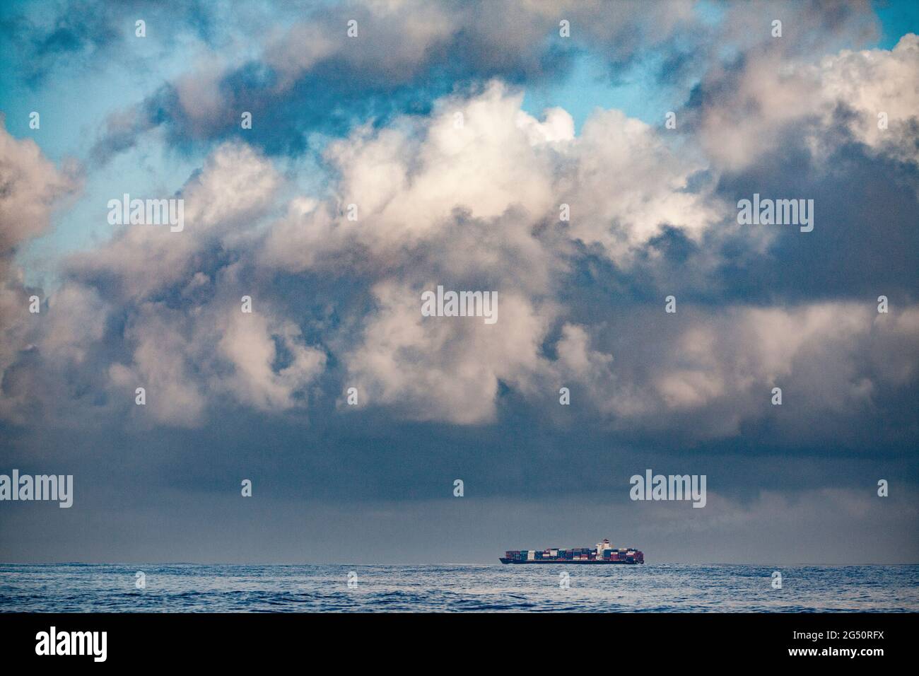 Riesiges Containerschiff in den Weiten des pazifischen Ozeans mit dramatischer Wolkenlandschaft eines bevorstehenden Sturms Stockfoto