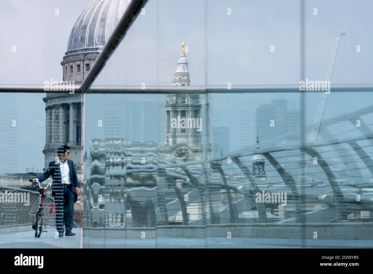 Mit der Kuppel der St. Paul's Cathedral in der Ferne schiebt ein Radfahrer am 24. Juni 2021 in London, England, sein Fahrrad über die Themse auf der Millennium Bridge. Londons neueste Flussüberquerung seit über 100 Jahren fiel mit dem Millennium zusammen. Sie wurde am 10. Juni 2000 in aller Eile fertiggestellt und für die Öffentlichkeit zugänglich gemacht, als schätzungsweise 100,000 Menschen sie überquerten, um zu entdecken, dass die Struktur so stark oszillierte, dass sie 2 Tage später geschlossen werden musste. In den nächsten 18 Monaten fügten Designer Dämpfer hinzu, um das Wackeln zu stoppen, aber es symbolisierte bereits das, was peinlich war und im britischen Stolz versagte. Jetzt t Stockfoto