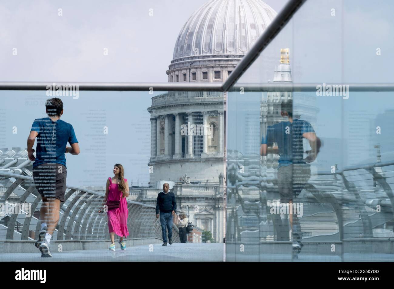 Mit der Kuppel der St. Paul's Cathedral in der Ferne überquert eine Frau in purpurrotem Kleid am 24. Juni 2021 in London, England, die Themse auf der Millennium Bridge. Londons neueste Flussüberquerung seit über 100 Jahren fiel mit dem Millennium zusammen. Sie wurde am 10. Juni 2000 in aller Eile fertiggestellt und für die Öffentlichkeit zugänglich gemacht, als schätzungsweise 100,000 Menschen sie überquerten, um zu entdecken, dass die Struktur so stark oszillierte, dass sie 2 Tage später geschlossen werden musste. In den nächsten 18 Monaten fügten Designer Dämpfer hinzu, um das Wackeln zu stoppen, aber es symbolisierte bereits das, was peinlich war und im britischen Stolz versagte. Jetzt Stockfoto