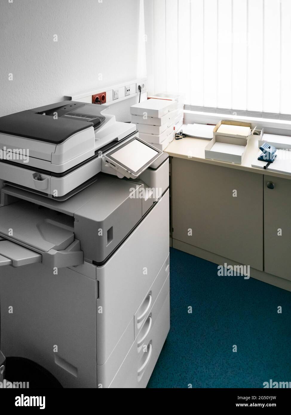 Typische Ecke in einem deutschen Büro. Ein großes Kopiergerät und viele Stapel Druckerpapier. Möbel und Teppich aus den 90er Jahren. Stockfoto