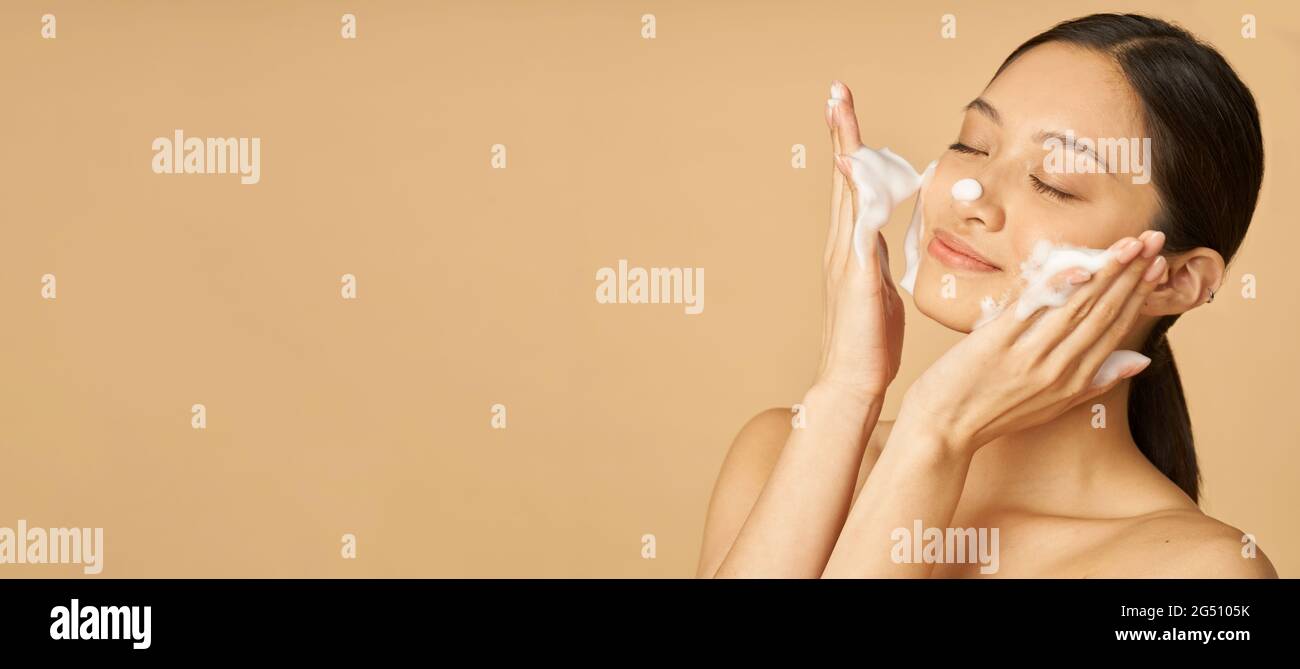 Website header of Beauty Portrait of happy Young Woman lachend with eyes closed while appling Gentle Foam facial Cleanser isolated over beige Stockfoto