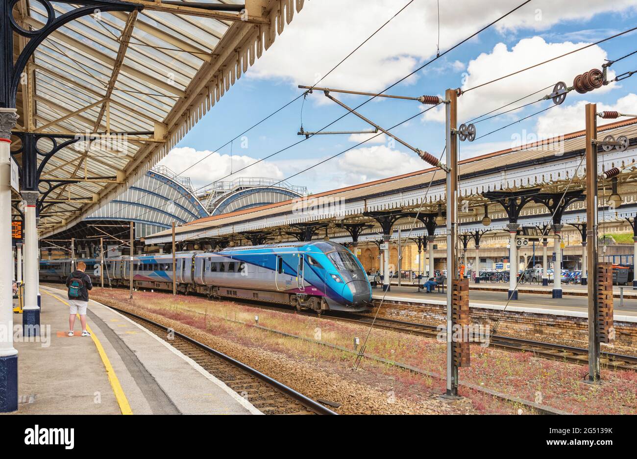 Am Bahnhofssteig steht eine schlanke, moderne Lokomotive. Ein Baldachin aus dem 19. Jahrhundert bedeckt die Plattform und ein junger Mann steht auf der Plattform. Stockfoto