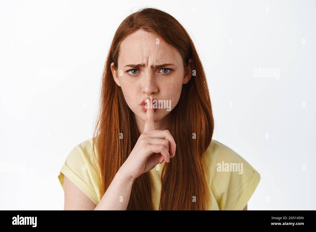 Nahaufnahme Porträt von wütenden Rotschopf teen Mädchen shushing, sagen shh, sagen, ruhig zu sein, Stirnrunzeln und schimpfen Person Fehlverhalten, über weiß stehen Stockfoto