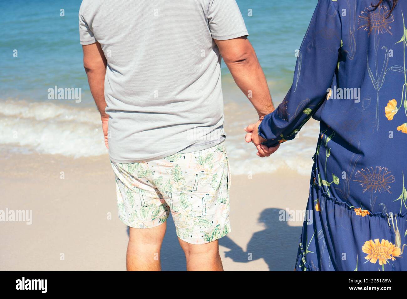 Ein älteres Paar stand Hand in Hand mit dem Strand vor ihnen. Stockfoto