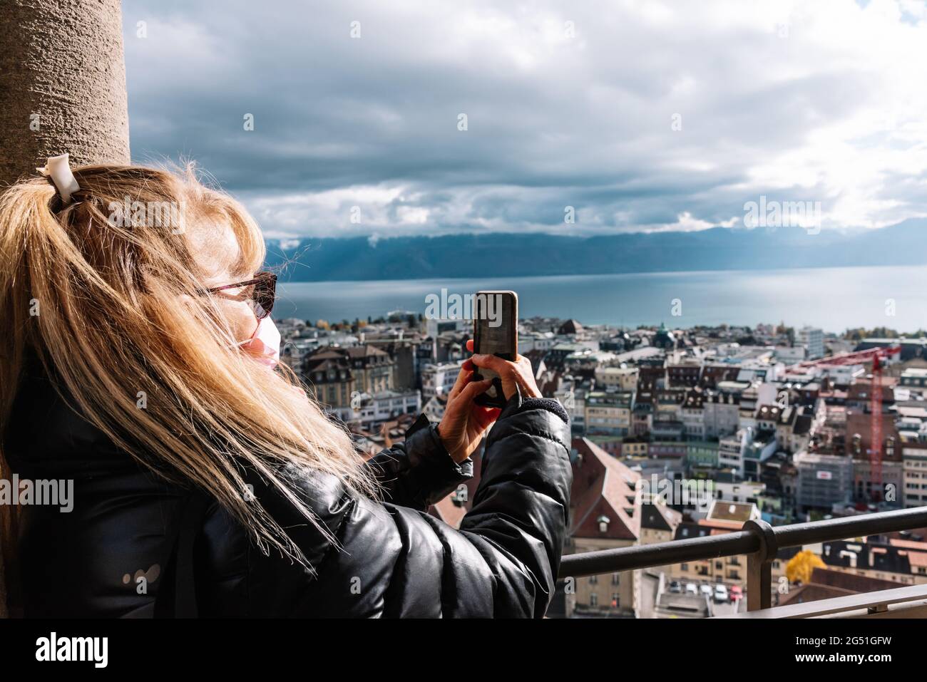 Unerkannte blonde Frau mit Gesichtsmaske, die ein Foto einer urbanen Landschaft gemacht hat. Stockfoto