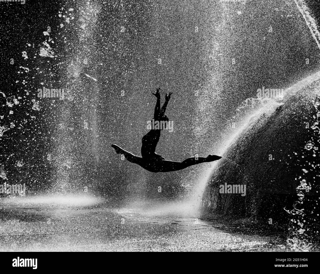 Silhouette einer Frau, die akrobatische Sprünge gegen den Brunnen macht Stockfoto