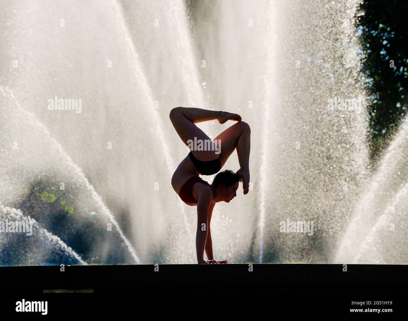 Silhouette einer Frau, die einen akrobatischen Handstand gegen einen Brunnen stellt Stockfoto