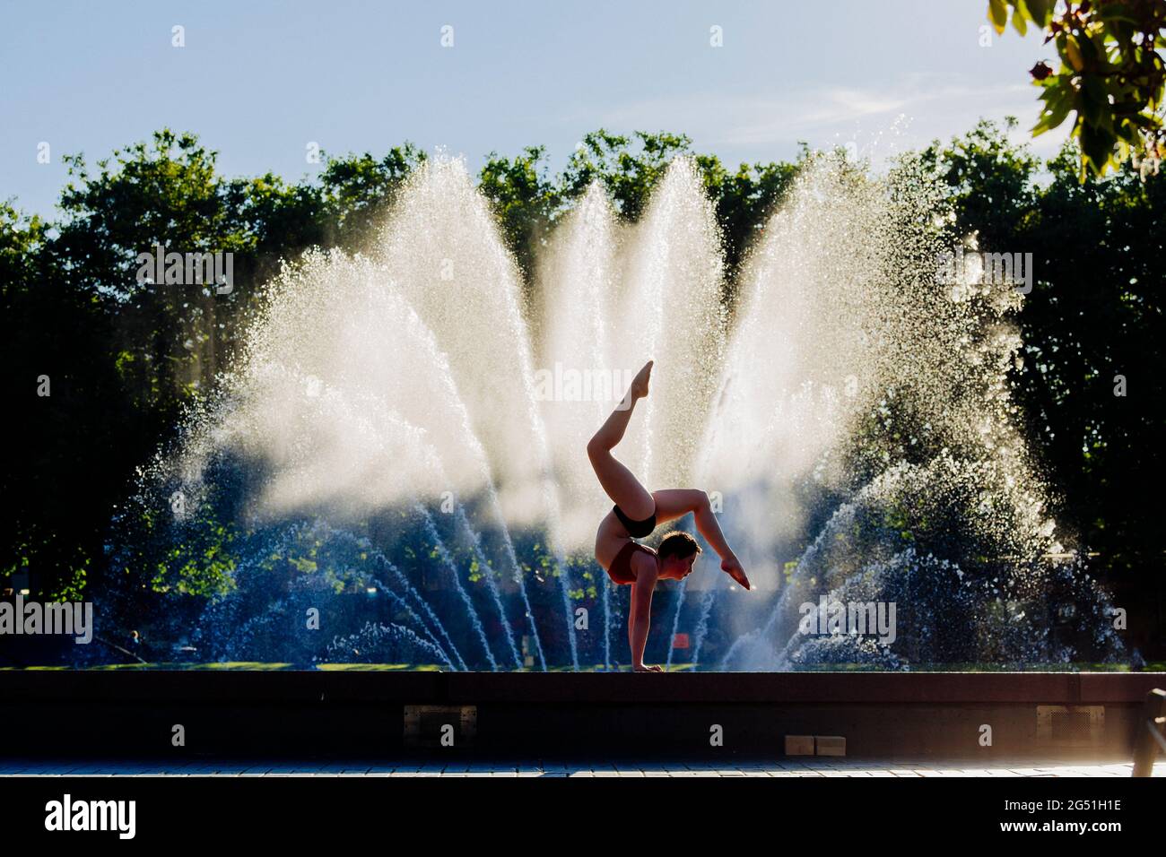 Frau mit akrobatischem Handstand stellt sich gegen den Brunnen Stockfoto