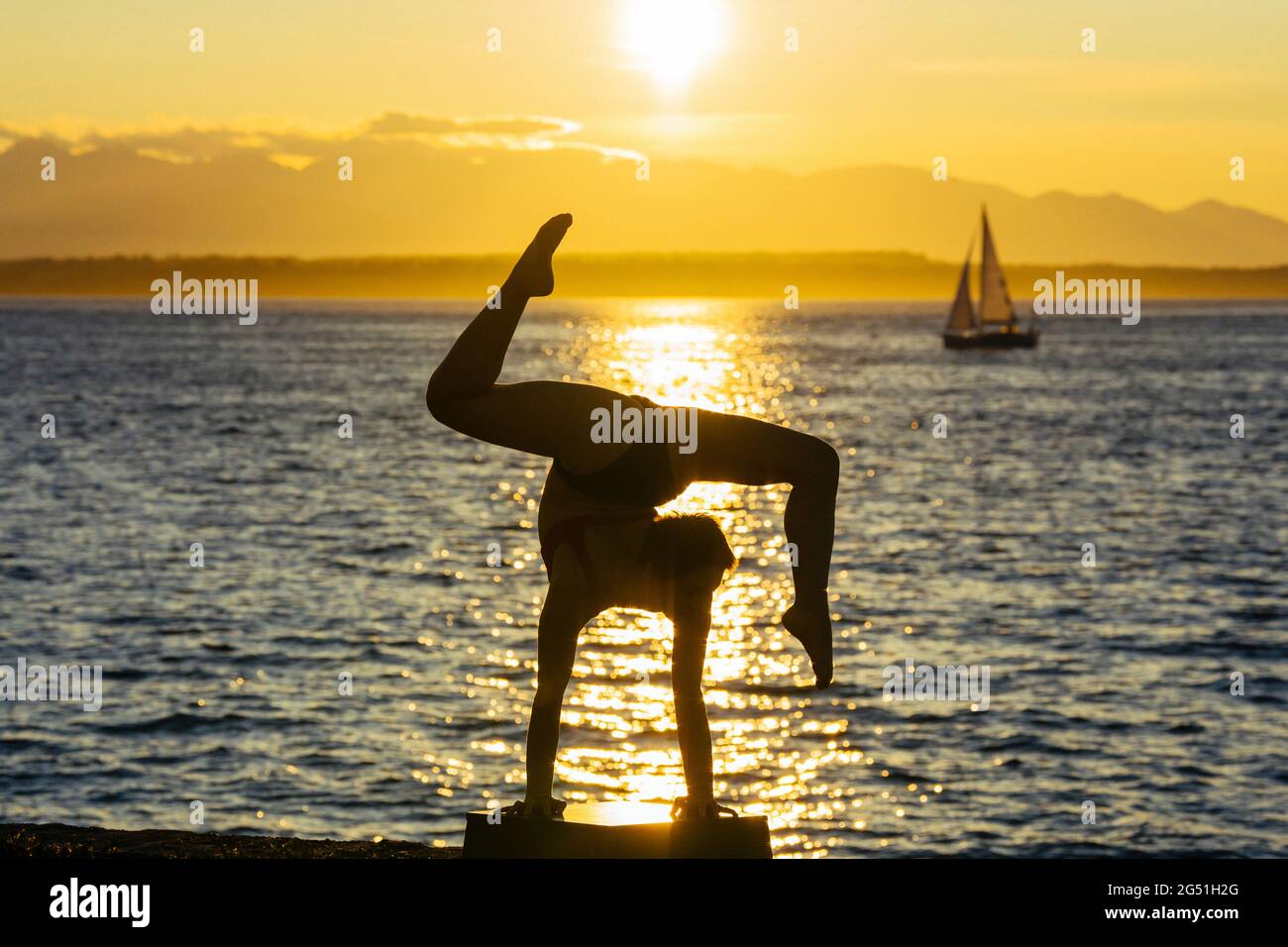 Silhouette einer Frau mit akrobatischem Handstand, die bei Sonnenuntergang gegen das Meer posiert Stockfoto