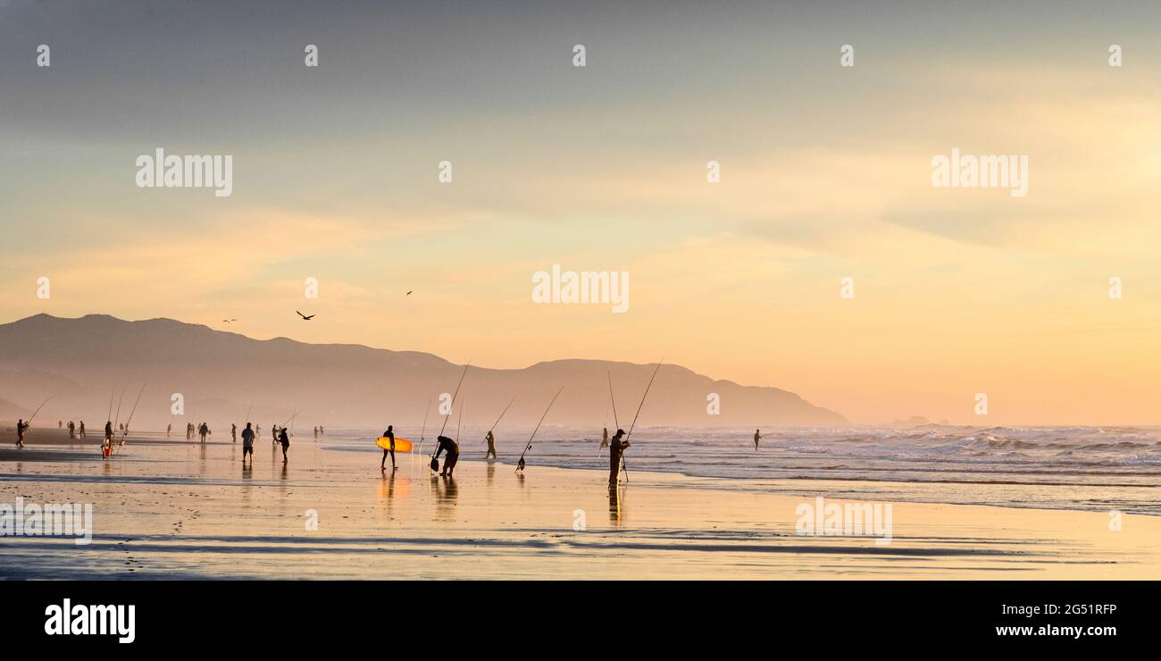 Gruppe von Fischern und Surfern am Strand bei Sonnenuntergang Stockfoto