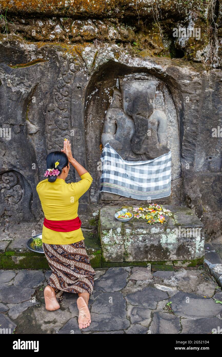 Frau, die am Ganesha-Altar in Yeh Pulu betet - Alte Reliefs in Desa Bedulu, Kabupaten Gianyar, Bali, Indonesien. Schnitzerei in der Felswand. Stockfoto