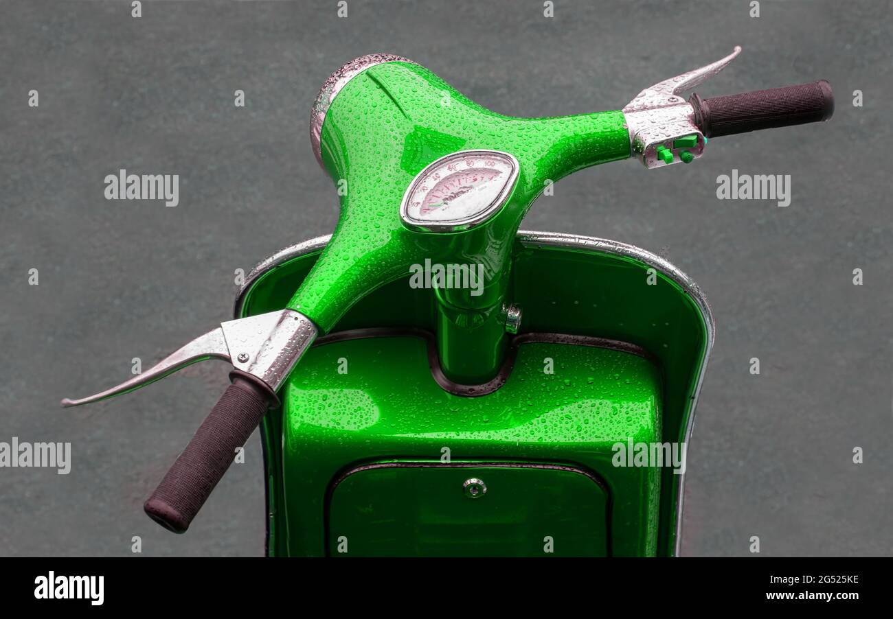 Ein leuchtend grüner Motorroller, der das Vorderteil aus der Sicht der Fahrer zeigt. Der Lack hat Wassertropfen aus dem Regen Stockfoto
