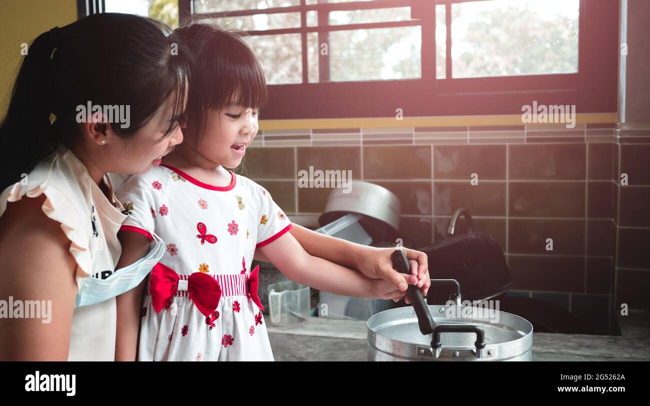 Mutter hält die Hand ihrer Tochter mit einer Pfanne, um die kochende Gelatine in einem Topf auf dem Küchengasherd zu schmelzen. Eine Mutter lehrt ihre Tochter zu machen Stockfoto