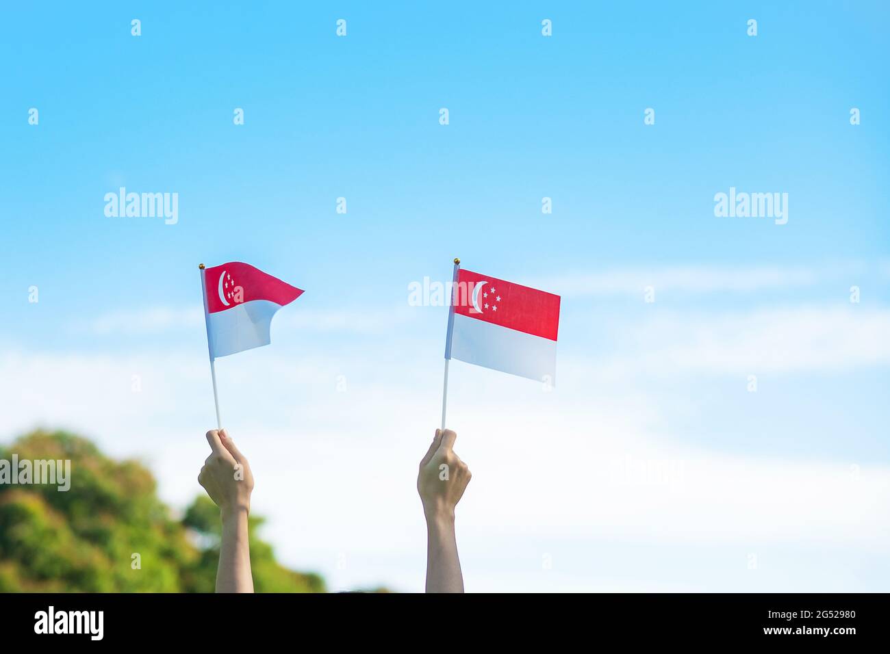 Hand mit Singapur-Flagge auf blauem Himmel Hintergrund. Singapore National Day und Happy Celebration Konzepte Stockfoto