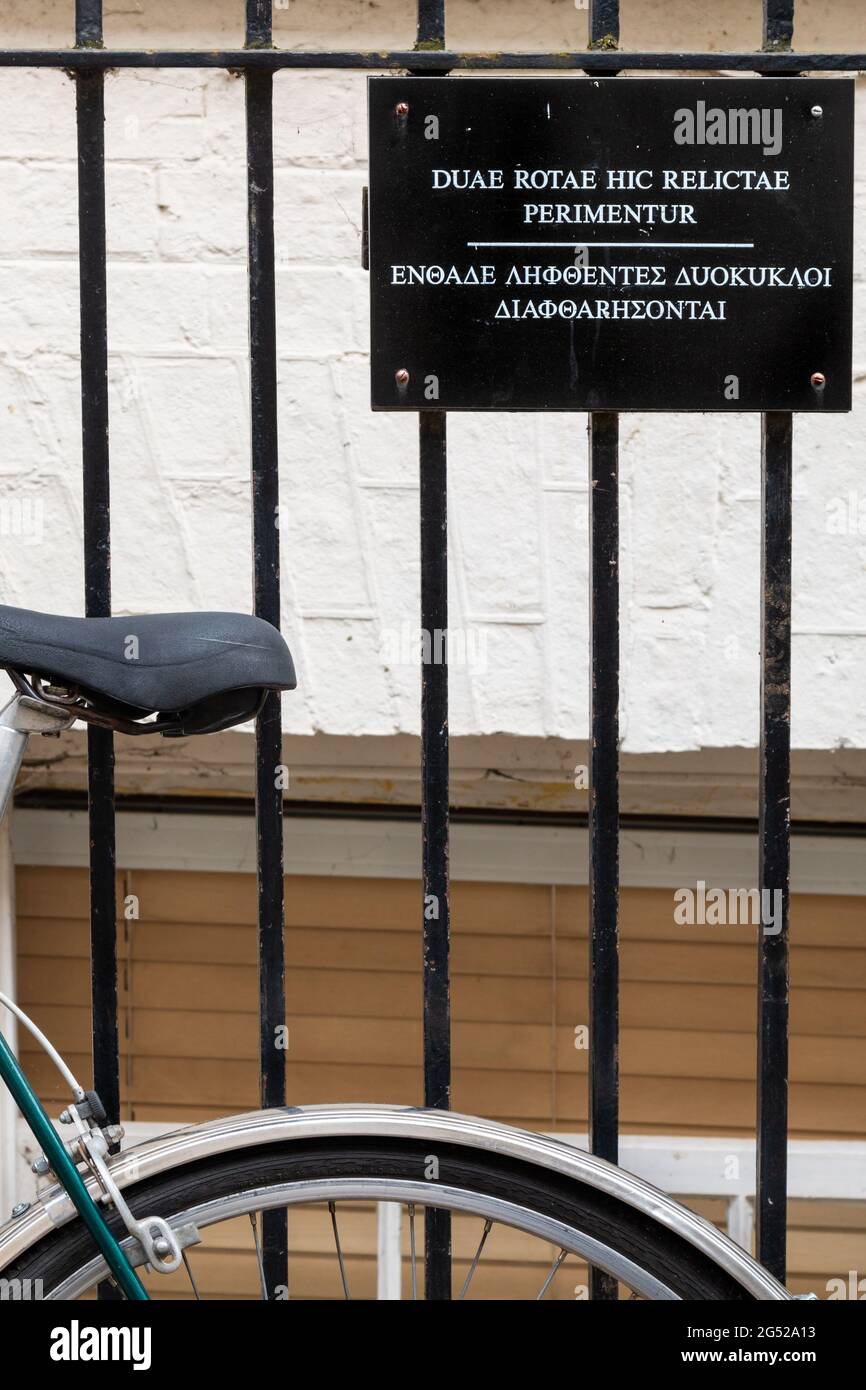 Ein Fahrrad ist an einen Zaun neben einem Schild angekettet, auf dem die Leute aufgefordert werden, ihre Fahrräder dort nicht in lateinischer und griechischer Sprache zu parken. Cambridge, Großbritannien Stockfoto