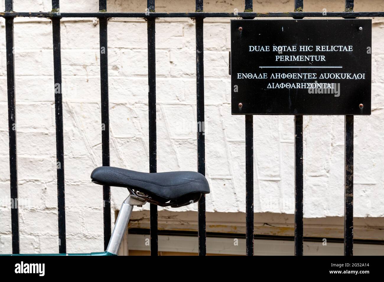 Ein Fahrrad ist an einen Zaun neben einem Schild angekettet, auf dem die Leute aufgefordert werden, ihre Fahrräder dort nicht in lateinischer und griechischer Sprache zu parken. Cambridge, Großbritannien Stockfoto