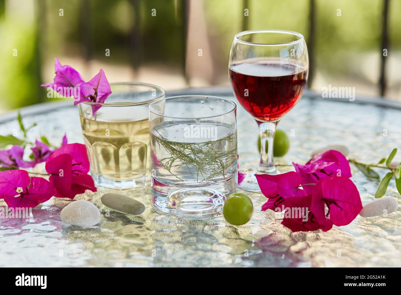 Sommerhausgemachte Cocktails und ein Glas Rotwein und rosa Blumen von Bougainvillea Dekorationen mit Kieselsteinen. Sommer Tapete aus nächster Nähe. Stockfoto