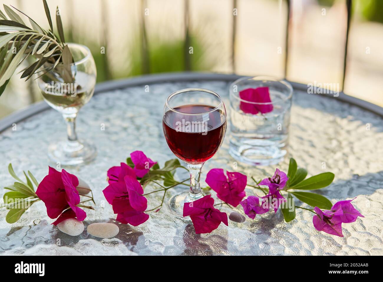 Sommercocktails und ein elegantes Glas Rotwein. Dekorative rosa Blumen und der Zweig des Olivenbaums im Glas. Glyphe der Reinigung. Draufsicht, Cop Stockfoto