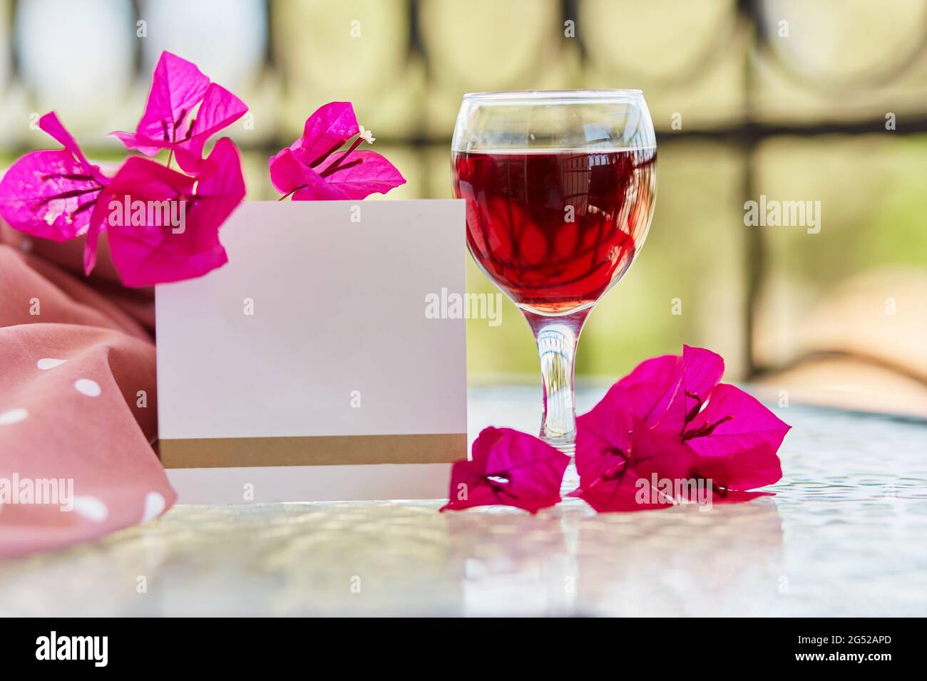 Elegantes Glas Rotwein. Dekorative rosa Blüten von Bougainvillea. Nachbau einer Postkarte oder Einladung. Festlich-romantisches Urlaubskonzept Stockfoto