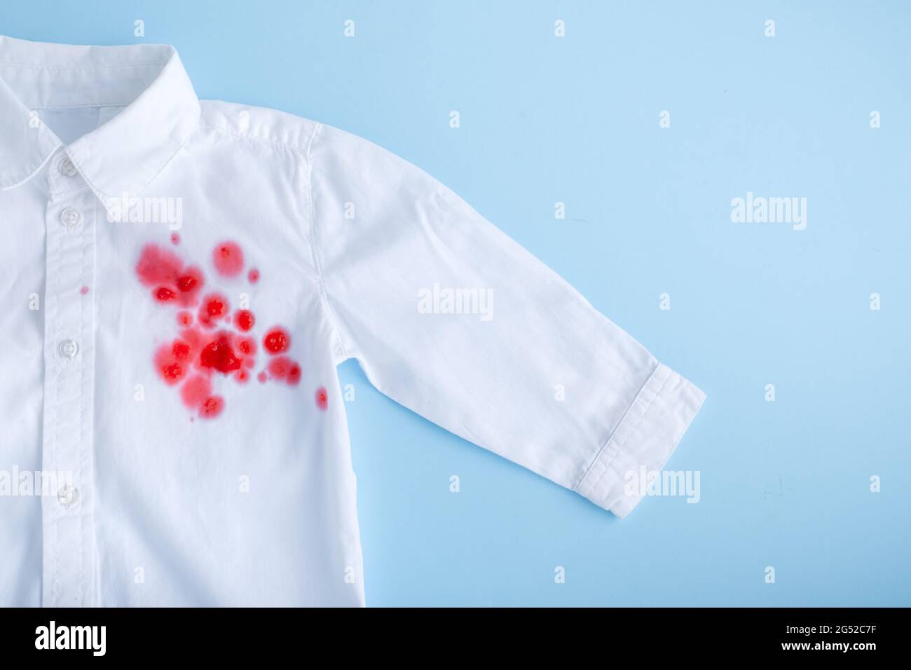 Verschütten Sie Getränke auf der Kleidung. Leuchtend rosa Fleck auf einem weißen Hemd von vorne. Isoliert auf blauem Hintergrund Stockfoto
