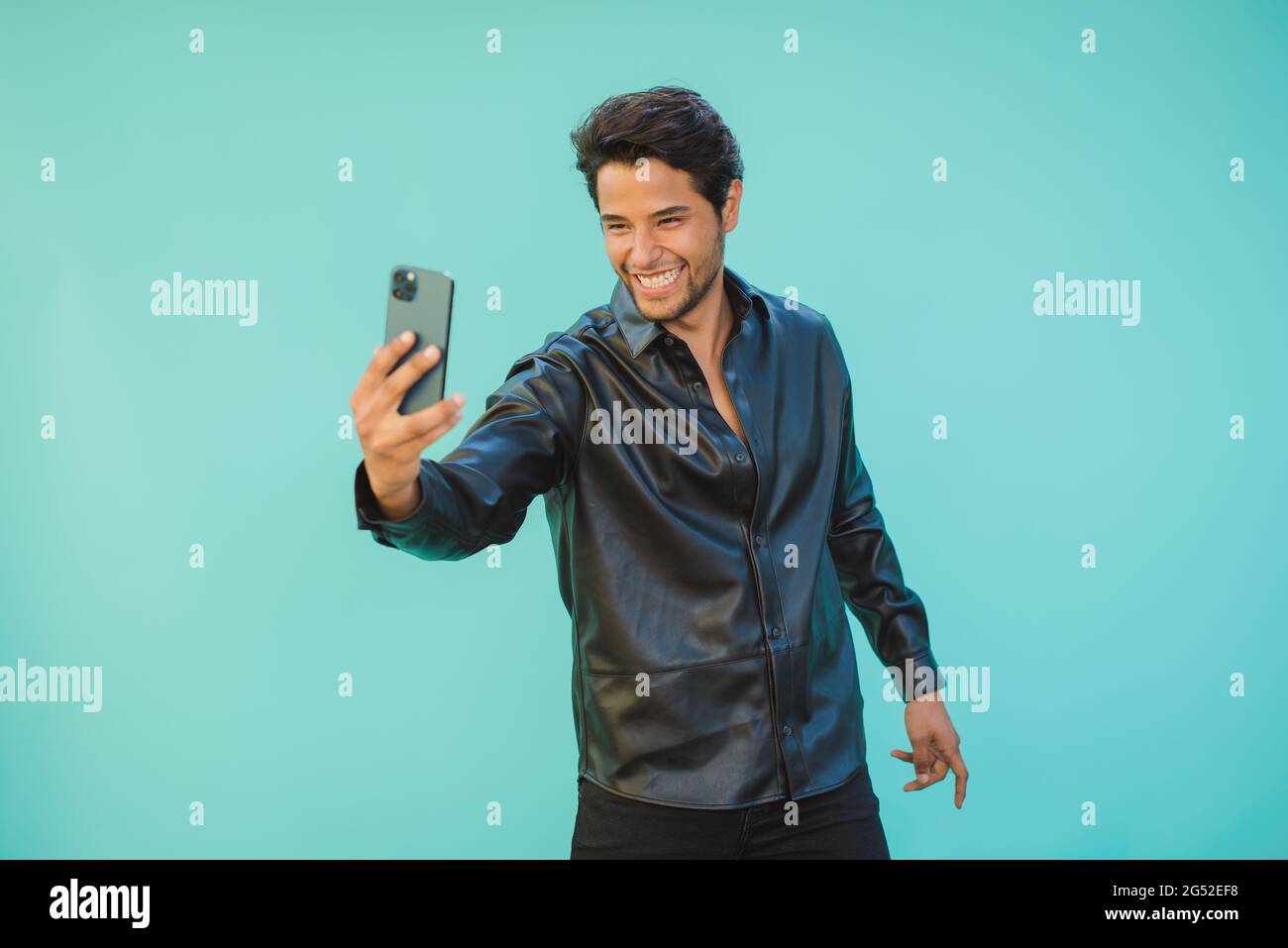 Glücklicher Mann, der Selfie auf dem Smartphone auf aquamarinfarbenem Hintergrund macht Stockfoto