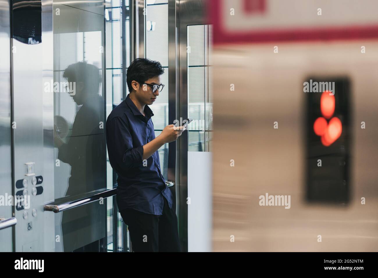 Hände eines jungen asiatischen Mannes, der ein Smartphone benutzt, im Aufzug Stockfoto