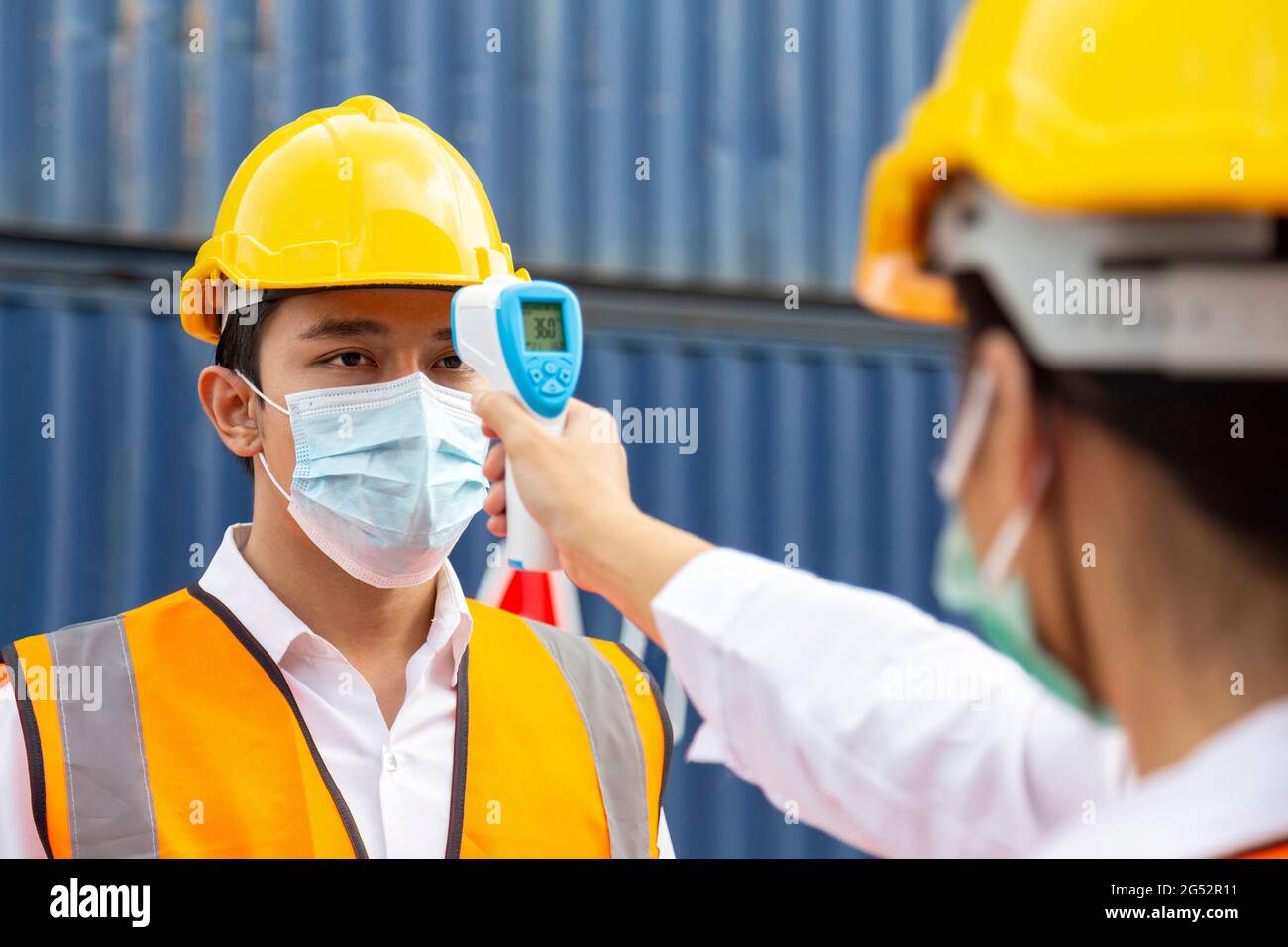 asiatischer Arbeiter mit Gesichtsmaske, der Fieber mit einem Digitalthermometer überprüft, bevor er die Arbeit zum Schutz vor Covid, Covid-19 oder Coronavirus p betreten hat Stockfoto