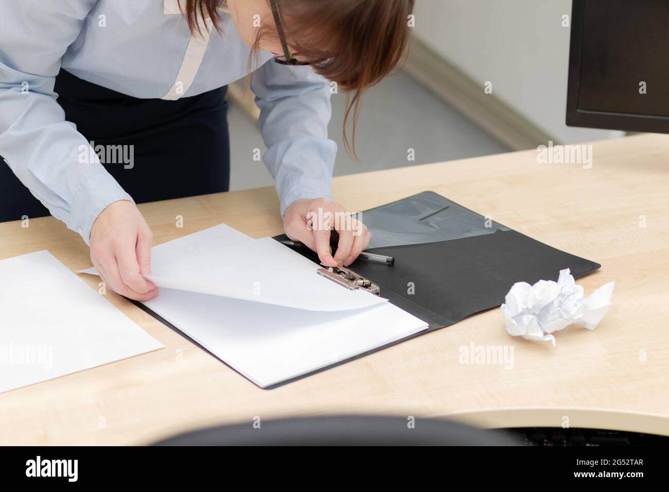 Weibliche Hände in einer blauen Bluse im Büro bei Ein Arbeitstisch aus Holz sieht in schwarz durch Dokumente Ordner Stockfoto