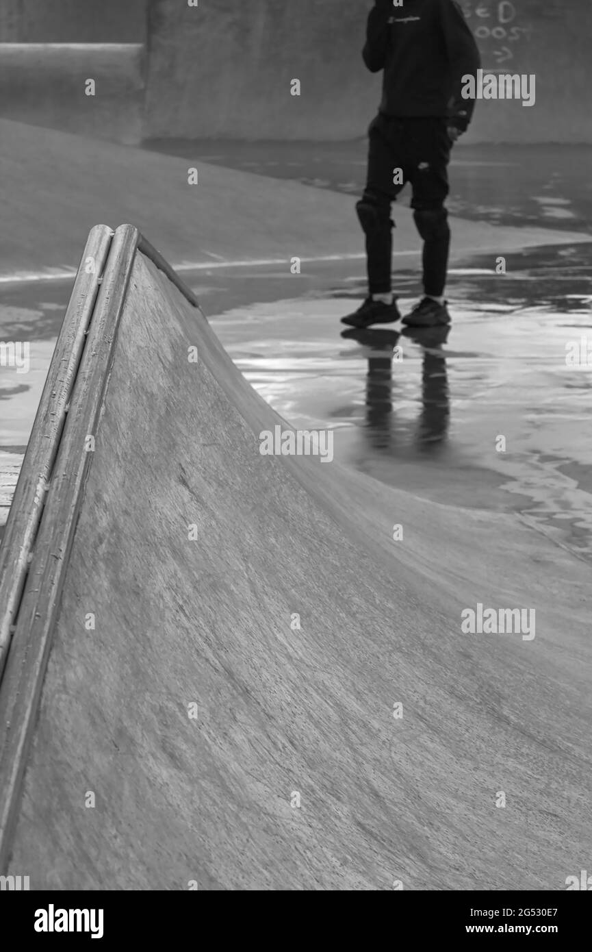 Junger Mann, der an EINEM regnerischen Tag in den Pfützen eines Concrete Skate Park in England spazierengeht Stockfoto