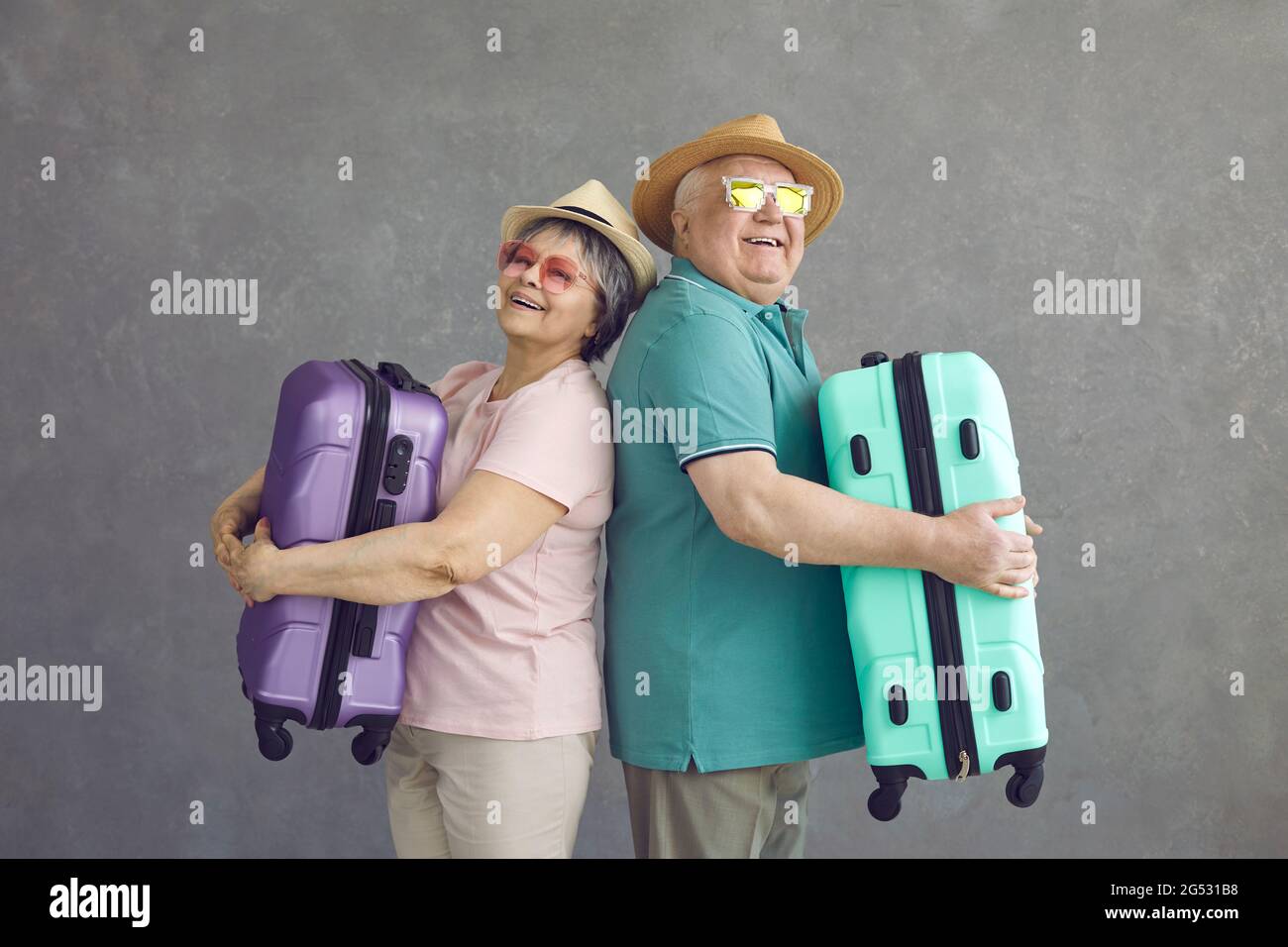 Studioportrait von glücklichen älteren Touristen, die Rücken an Rücken stehen und Koffer halten Stockfoto