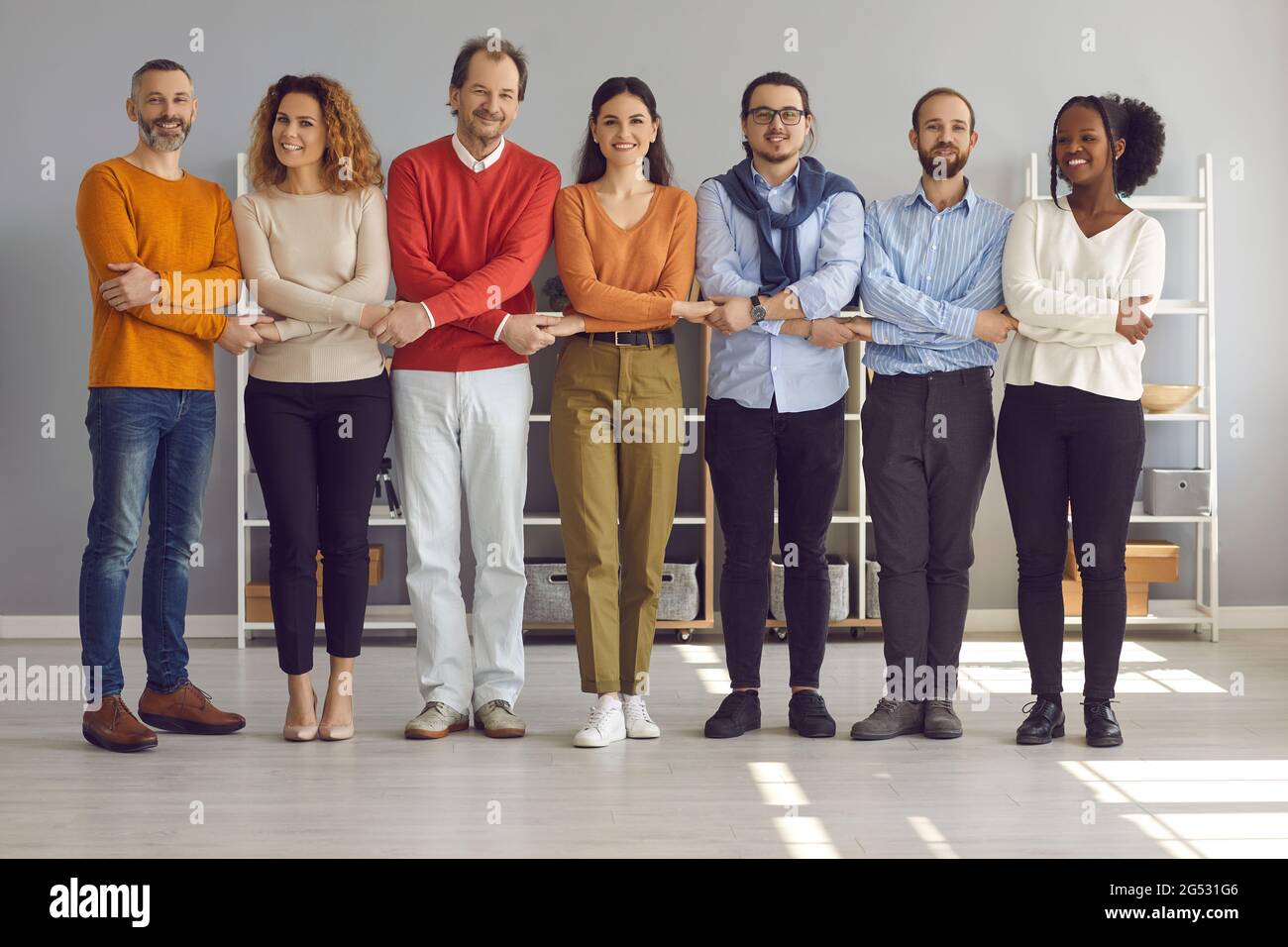 Glückliche, multiethnische Menschen, die die Hände zusammenhalten und die Kamera betrachten, stehen in Reihe Stockfoto