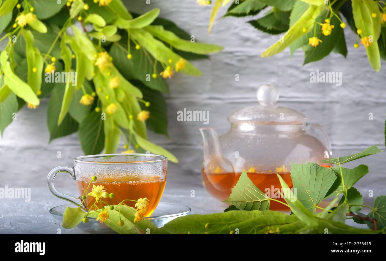 Vor dem Hintergrund einer Ziegelwand, eine Teekannen und eine Tasse mit Lindentee und Blumen auf einem Holztisch Stockfoto