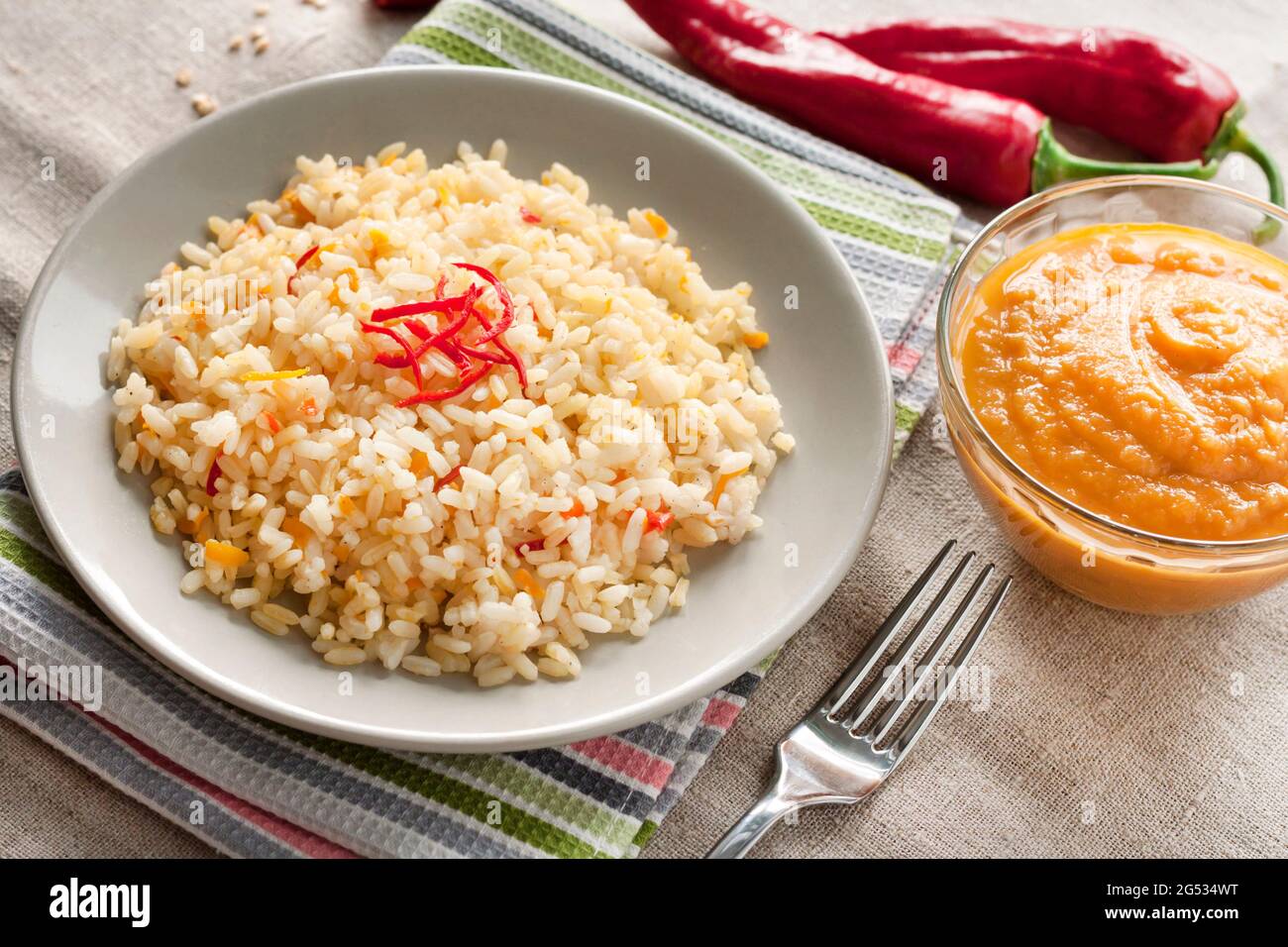 Würziger, parboilter Reis mit Karotten, gelben Zucchini und Chilischoten auf einem grauen Teller Stockfoto