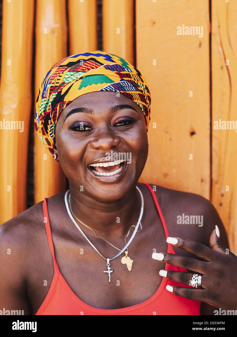 Afrikanische Frau mit einem hoffnungsvollen glücklichen Lächeln und traditionellem Kopfschmuck, die gegen eine bemalte Holzwand im tropischen Dorf Keta Ghana West A steht Stockfoto