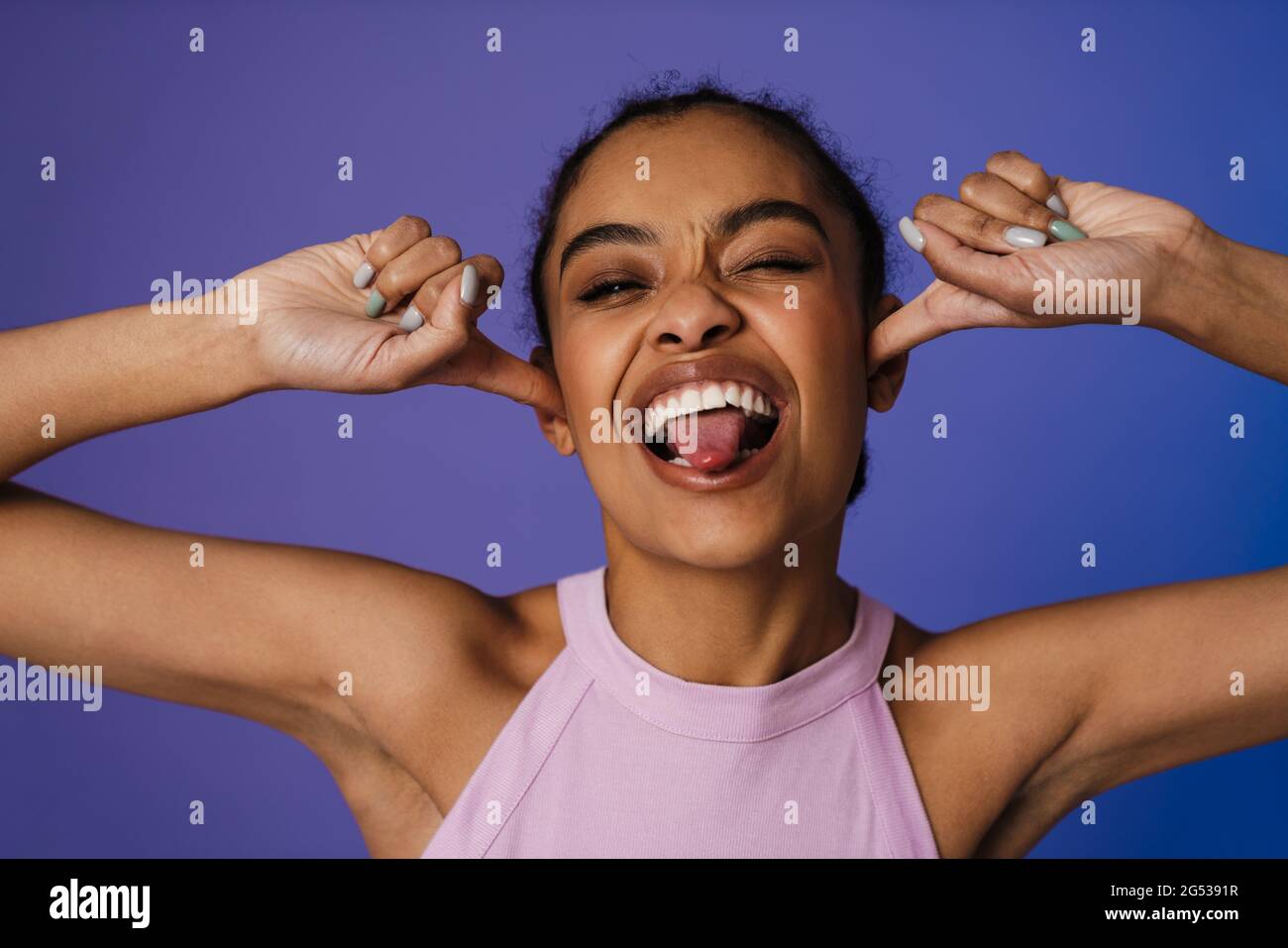 Glückliche junge afrikanische Frau, die über blauem Wandhintergrund steht, witziges Grimassen Stockfoto