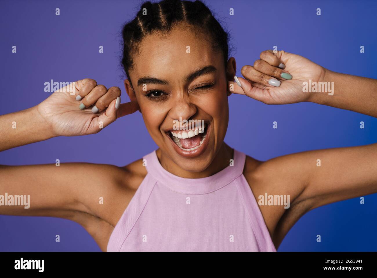 Glückliche junge afrikanische Frau, die über blauem Wandhintergrund steht, witziges Grimassen Stockfoto
