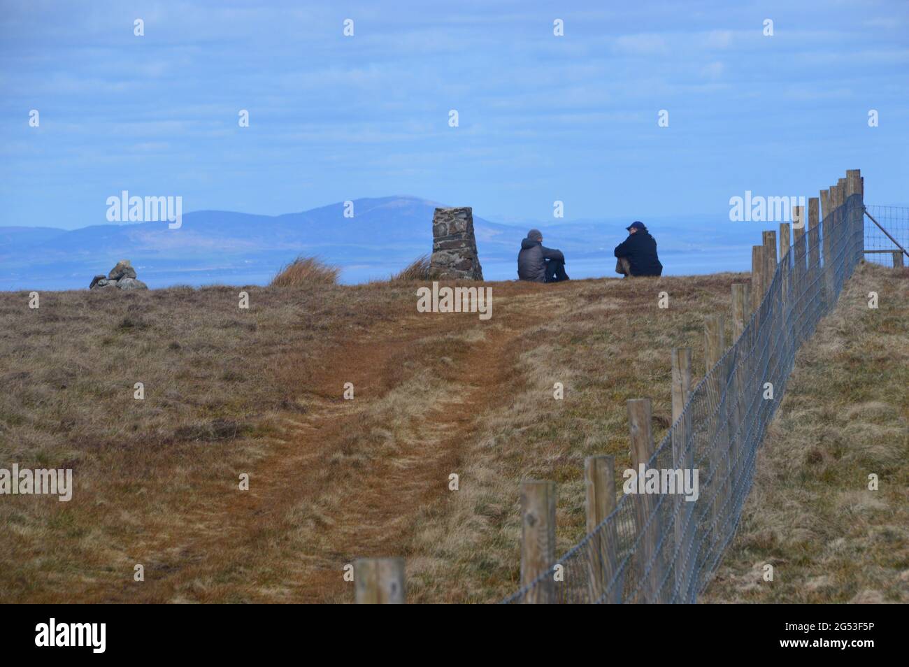 Two Men Sitting & Talking by the Stone Trig Point & Pile of Stones (Cairn) auf dem Gipfel des Wainwright 'Fellbarrow' Lake District, Cumbria, Großbritannien. Stockfoto