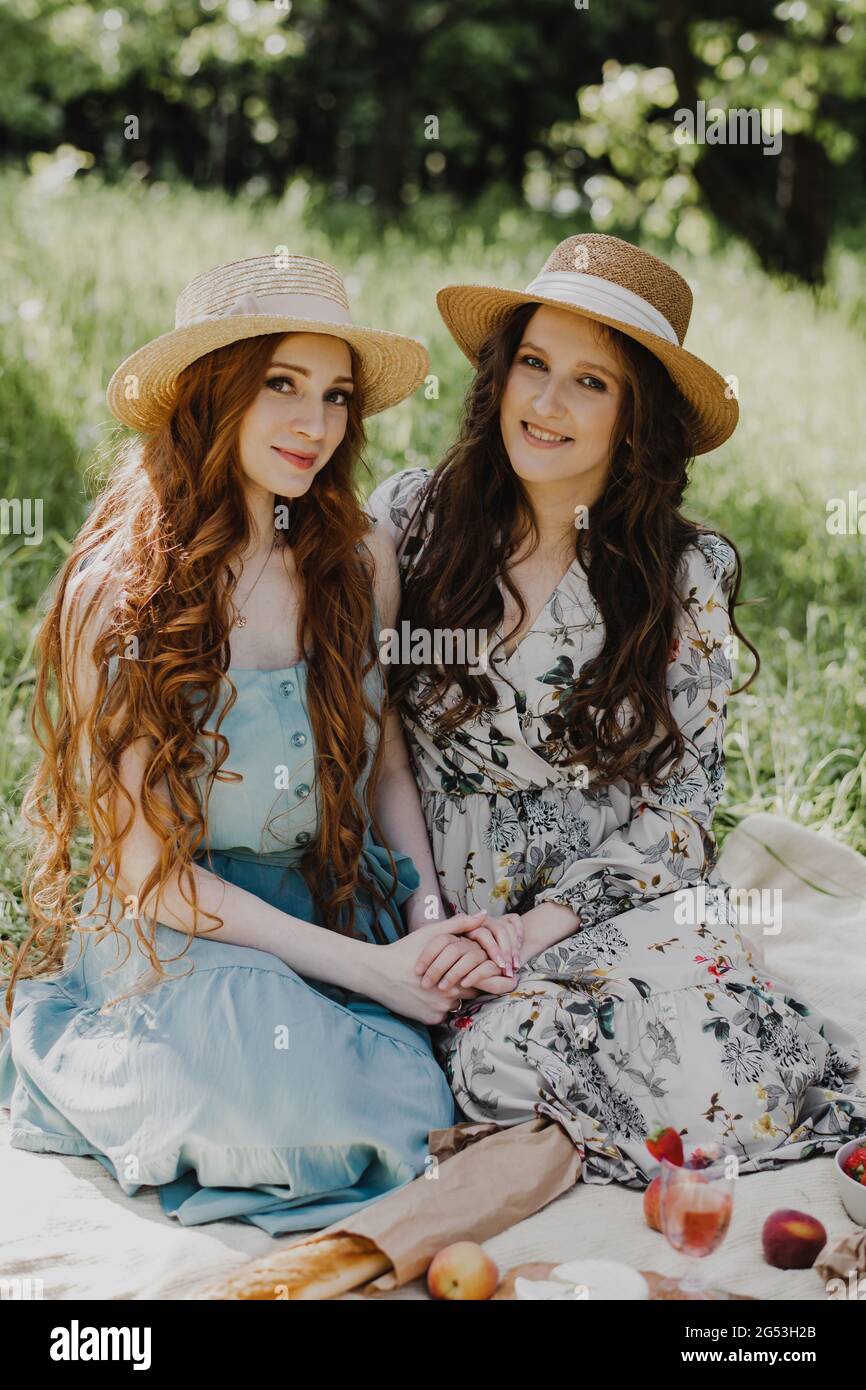 Zwei schöne Frauen in Sommerkleidern und Strohhüten genießen Picknick auf dem Land. Stockfoto