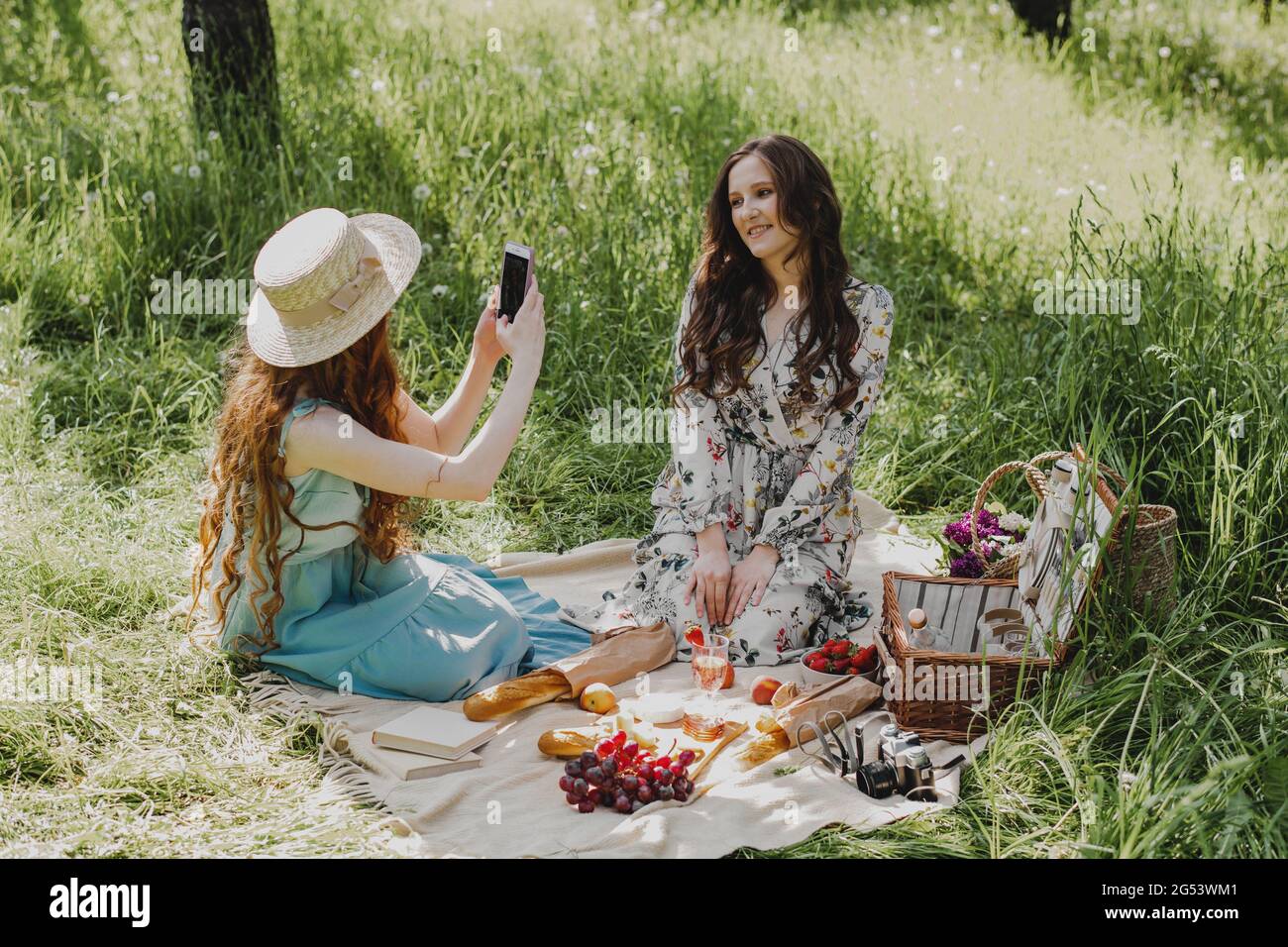 Glückliche Frau, die auf dem Smartphone beim Picknick im Freien Fotos von ihrer besten Freundin macht. Stockfoto