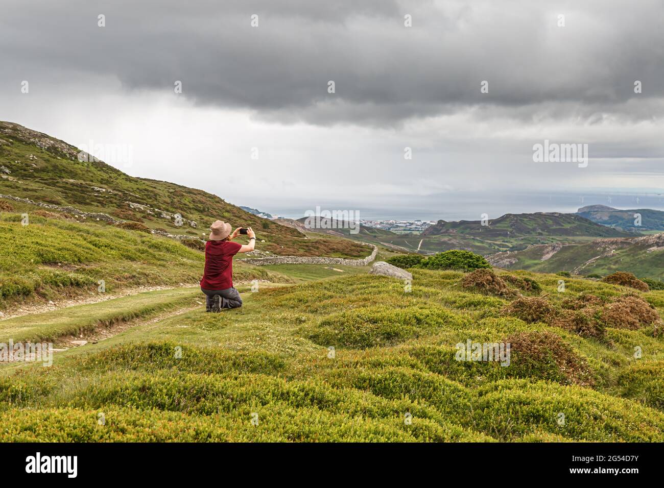 Eine einzige Wandererin, die mit einem Mobiltelefon Fotos auf dem Wales Coastal Path in Penmaenmawr, Cony, Wales, macht Stockfoto