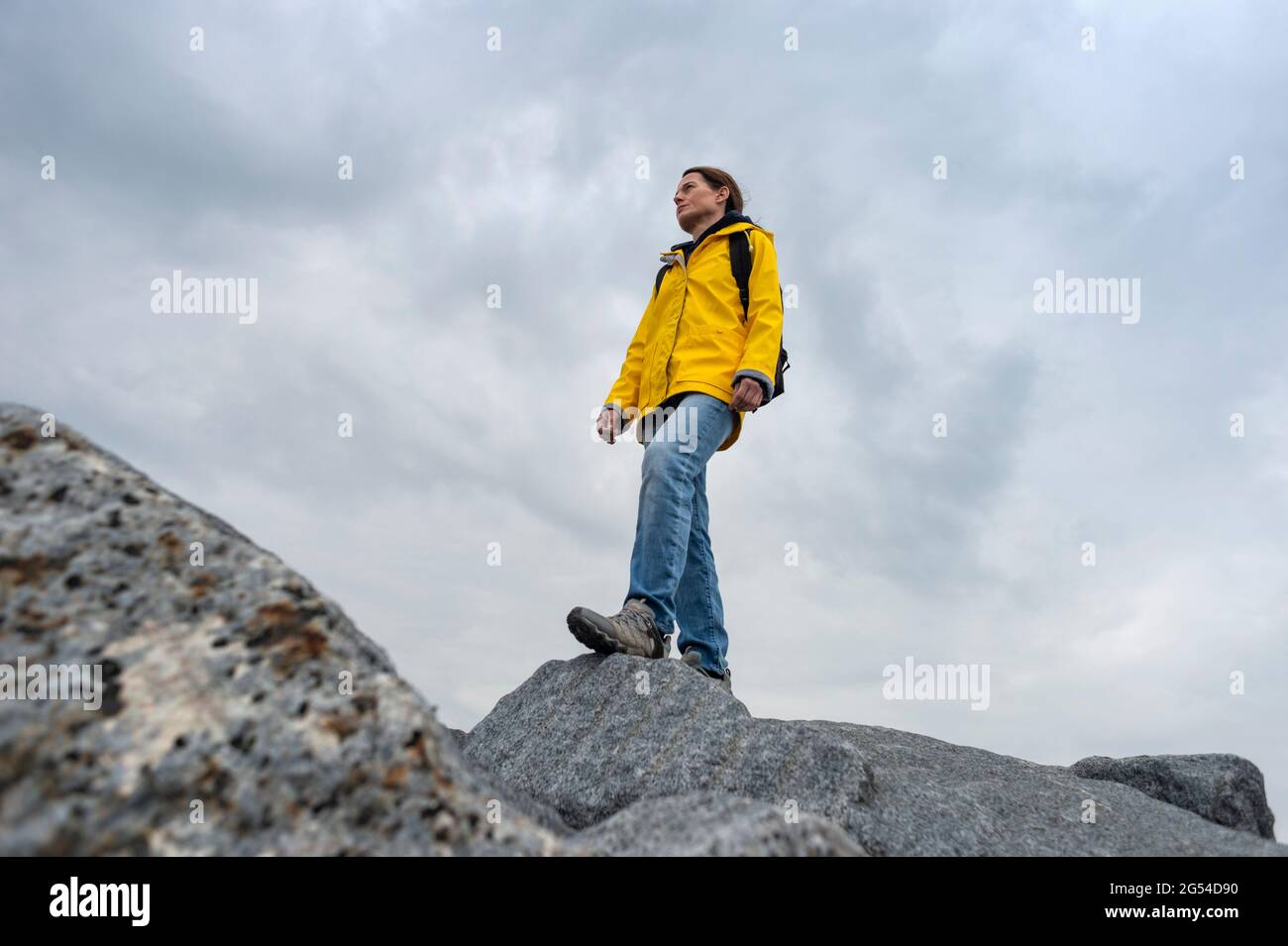 Frau mit gelbem Regenmantel, die auf Felsen steht und die Aussicht genießt. Backpacker erkunden. Stockfoto