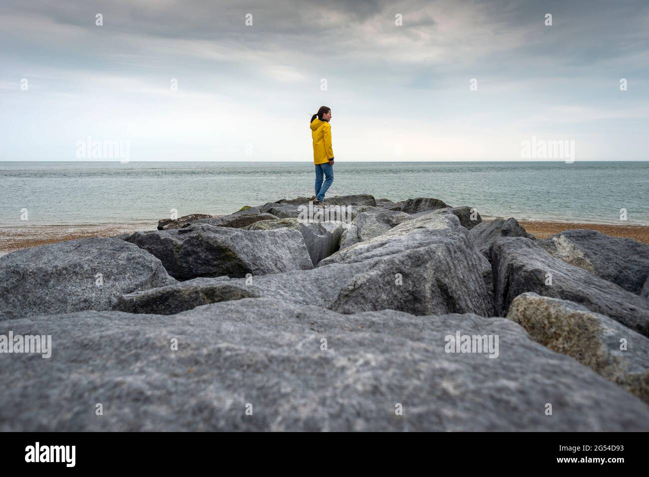 Frau in gelbem Regenmantel mit Blick auf das Meer, während sie auf Felsen steht Stockfoto