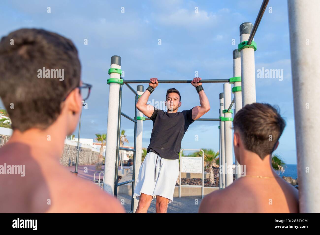 Ein junger Athlet trainiert mit Bars in einem Outdoor-Fitnessstudio und seine Freunde gucken und jubeln. Es ist Sommer und der Tag ist wunderschön Stockfoto