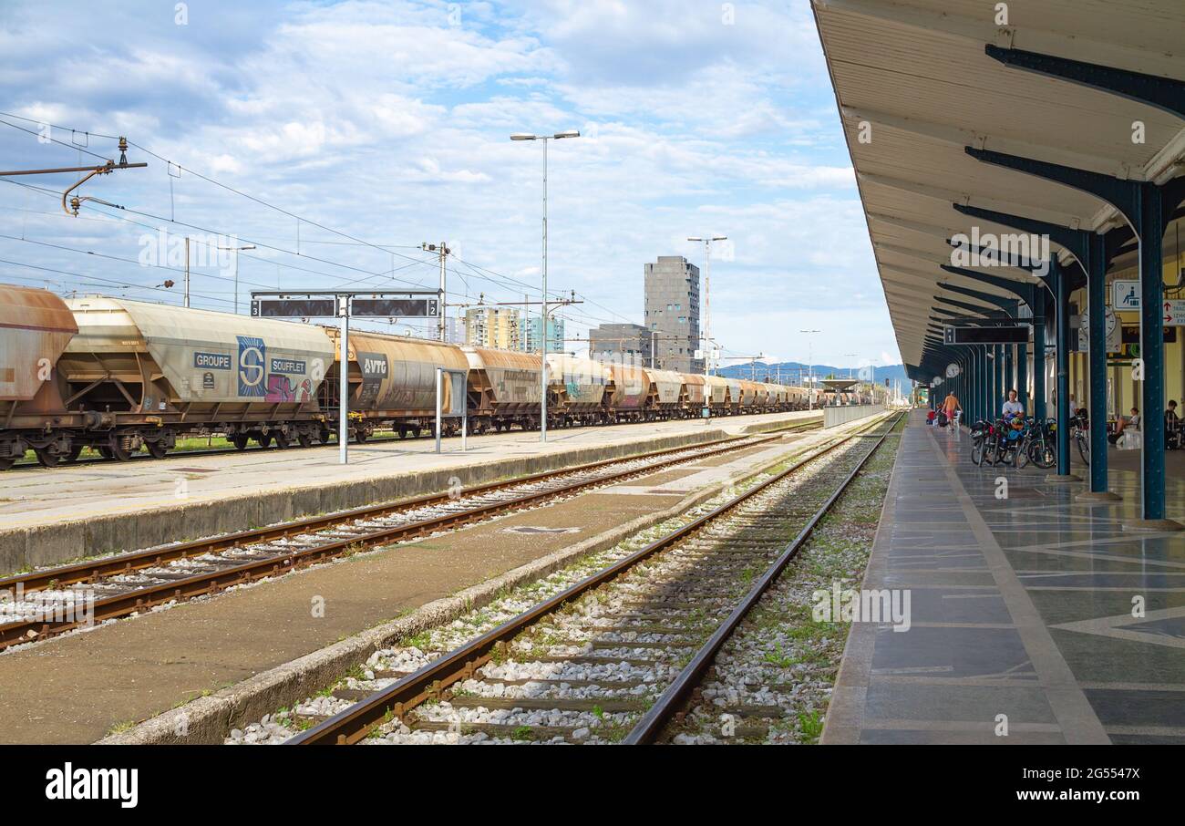 Ljubljana, Slowenien - 15. August 2018: Ein langer Güterzug fährt durch den Hauptbahnhof, während einige Passagiere auf ihren Transport warten Stockfoto