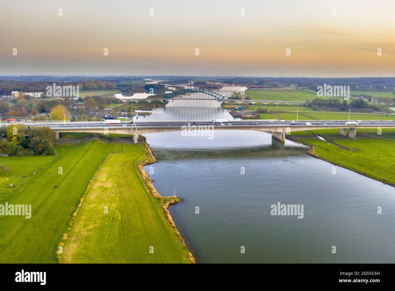 Luftaufnahme des riesigen Tieflandflusses IJssel mit Autobahn und Eisenbahnbrücken durch Sonnenuntergangslandschaft. Zwolle, Overijssel Provinz, Niederlande. Dro Stockfoto