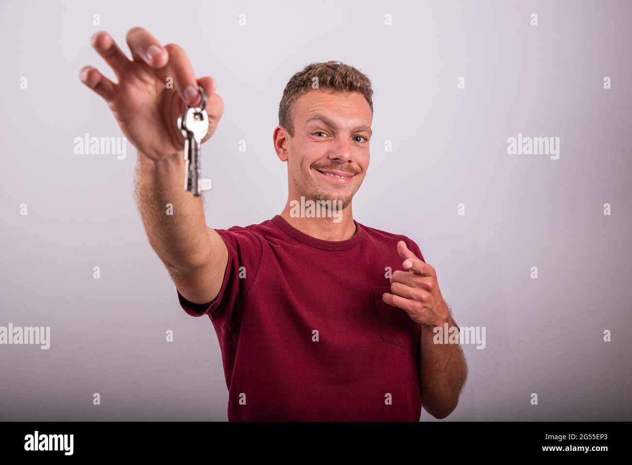 Ein auf weißem Hintergrund isolierter Junge hält Schlüssel in der Hand und zeigt auf sie, Werbefoto, Immobilienmakler-Konzept, Stockfoto