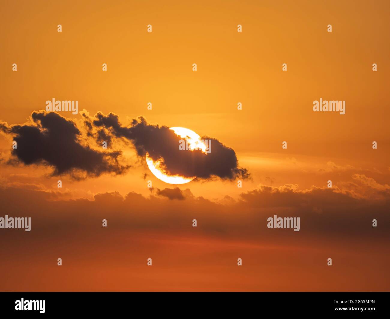 Sonne hinter kleinen Wolken in orangefarbenem Himmel bei Sonne Stockfoto