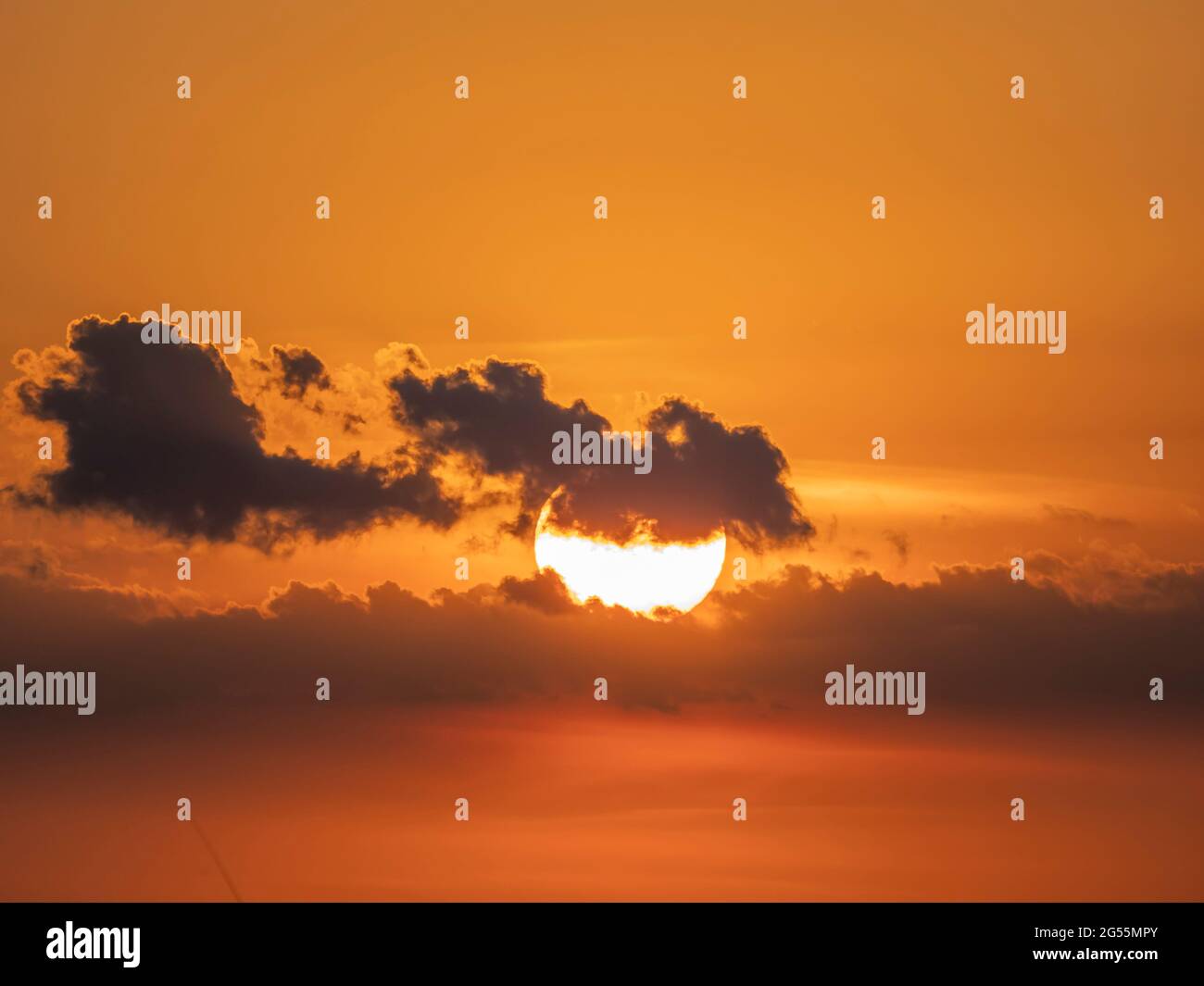 Sonne hinter kleinen Wolken in orangefarbenem Himmel bei Sonne Stockfoto